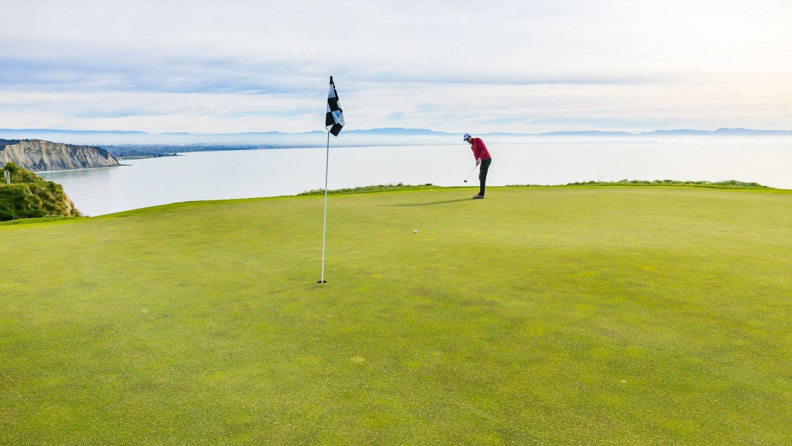 A golfer putting on a clifftop green above the sea at Cape Kidnappers, New Zealand